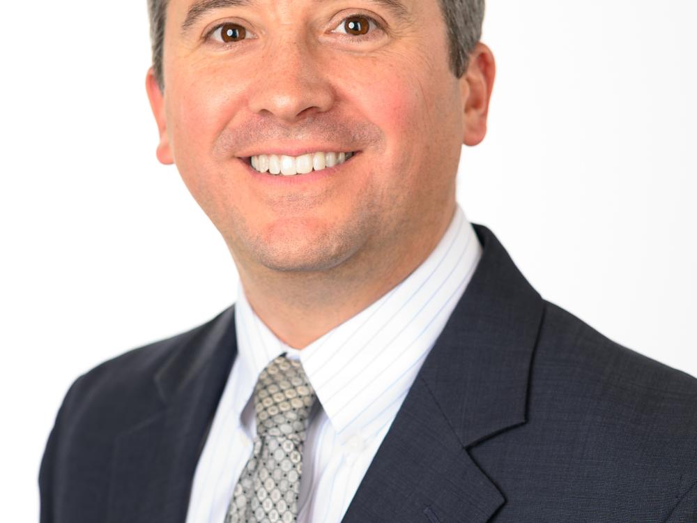 Headshot of a smiling man in a suit and tie against a plain white background.