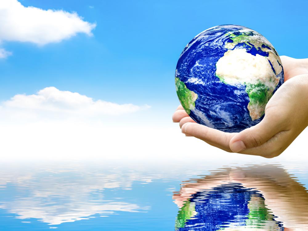 Two hands holding a small globe above water, reflecting the earth, with a blue sky and white clouds in the background.