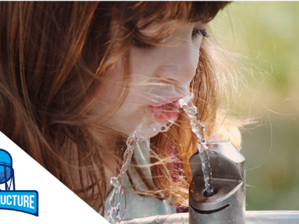 A young child drinks water from a fountain outdoors. The image includes the Aquastructure logo with a water tower icon.