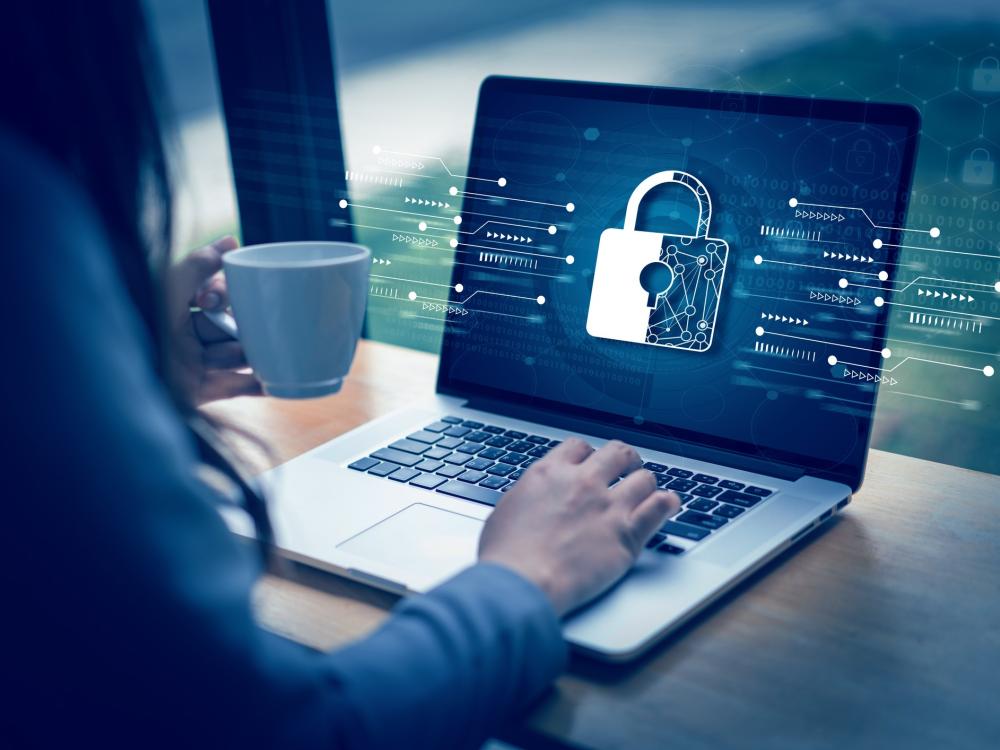 A person holds a coffee cup while working on a laptop displaying a digital lock icon, symbolizing cybersecurity and data protection.