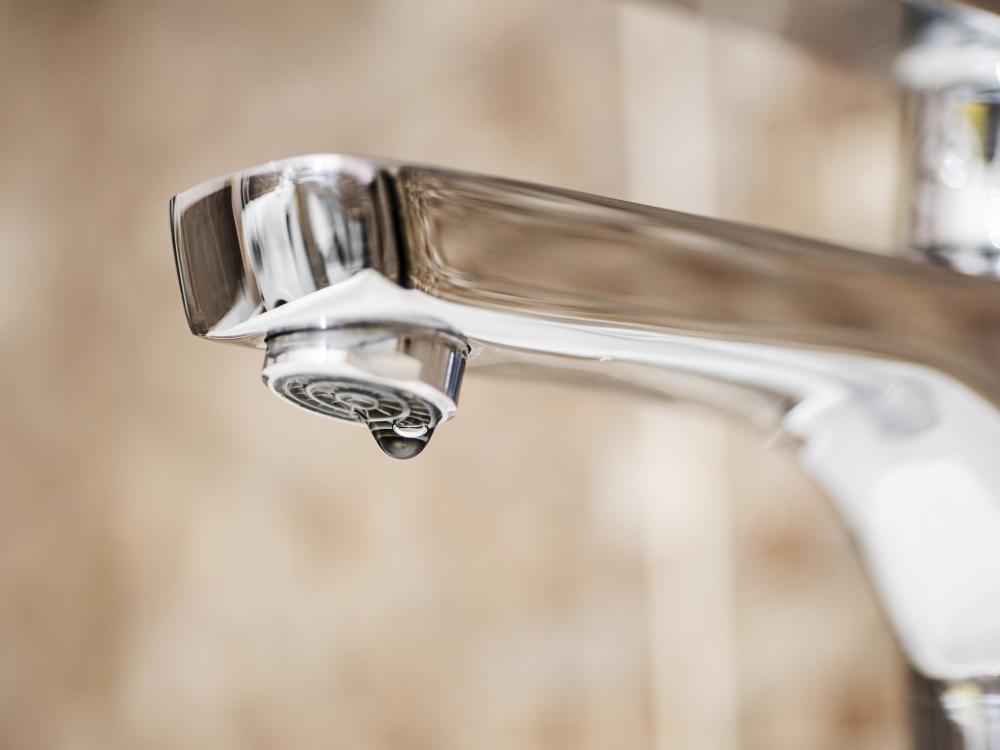 Close-up of a chrome faucet with a single water droplet forming, highlighting a potential leak against a blurred background.