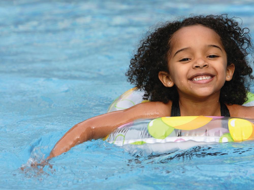 A smiling child in a colorful float enjoys playing in a swimming pool, surrounded by clear blue water.