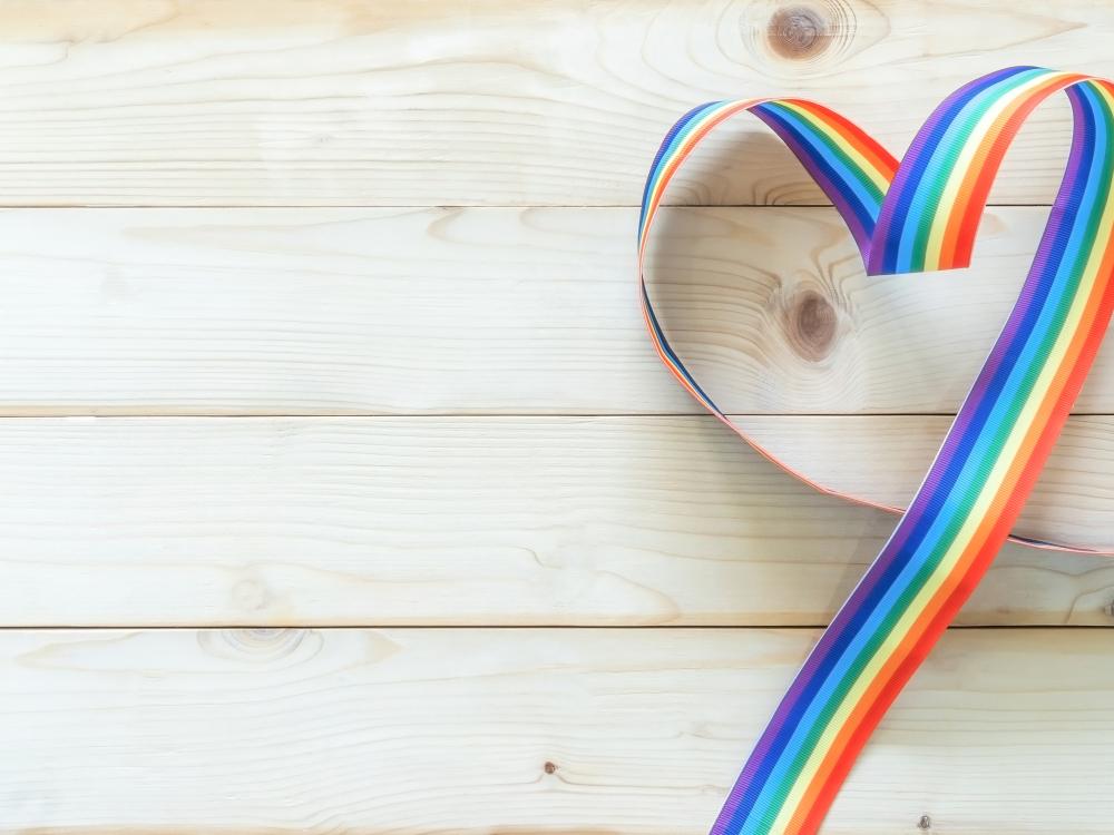 A rainbow ribbon shaped into a heart on a light wooden background.