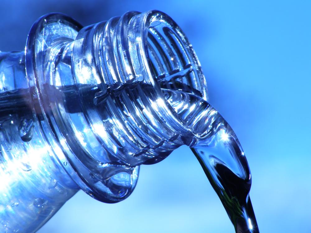  Close-up of water pouring from a clear plastic bottle against a bright blue sky background, with light reflecting off the surface.