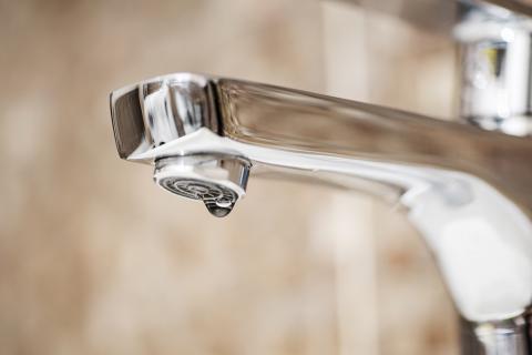 Close-up of a chrome faucet with a single water droplet forming, highlighting a potential leak against a blurred background.